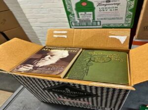 Cardboard box with flaps open to reveal books filling it to the top.