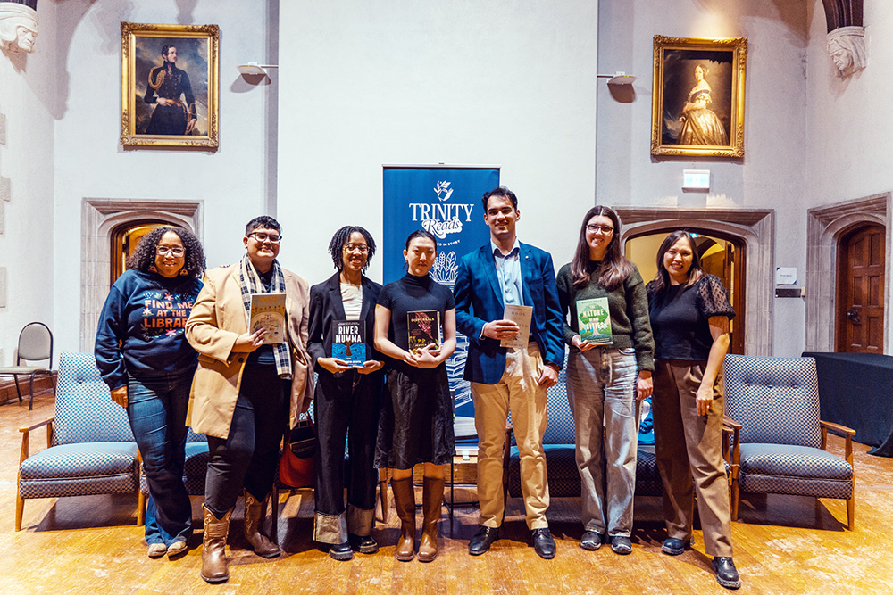 A group of people pose in Seeley hall with a Trinity Reads poster in the background