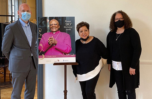 Chris Brittain, Carole Adriaans and Paige Souter stand with a poster of Archbishop Tutu