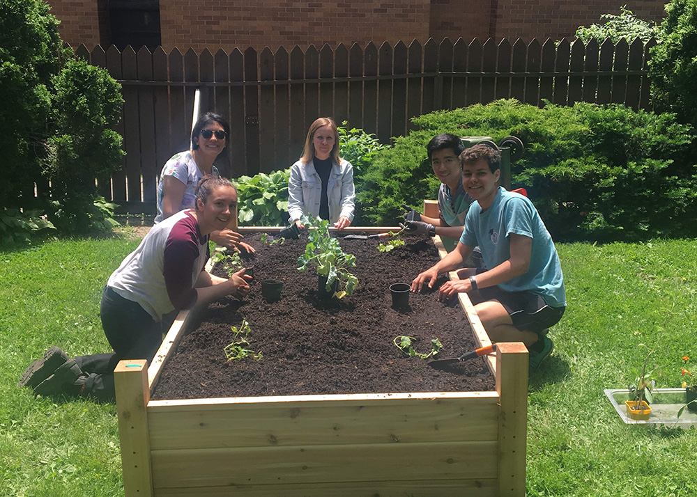 Raquel Serrano, Nicole Spiegelaar and student researcher set up a raise garden bed at St. Hilda's