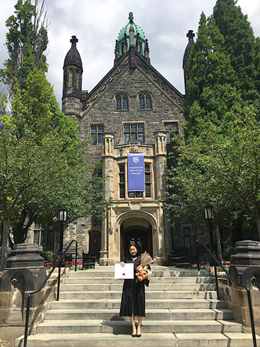 Maria Monica Layarda holding her diploma on the front steps of Trinity College building
